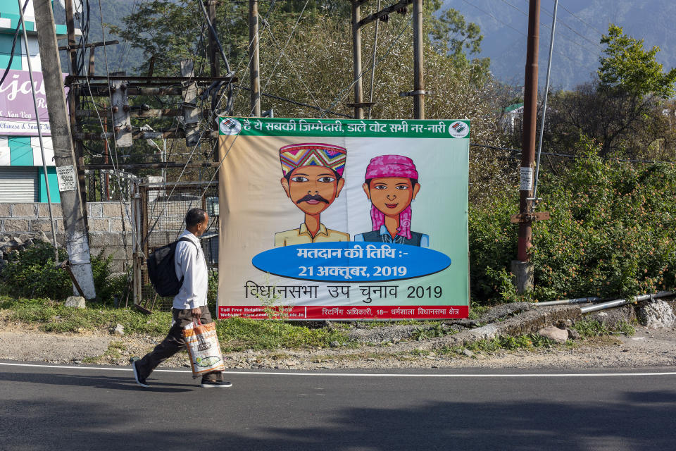 A man walks past a roadside hoarding announcing bypolls for an assembly seat in Dharmsala, India, Monday, Oct. 21, 2019. The seat was vacated by Kishan Kapoor, a BJP MLA, who was elected to the Lok Sabha in May, as Voting is underway in two Indian states of Maharashtra in the west and Haryana in the north where the Hindu nationalist Bharatiya Janata Party (BJP) headed by prime minister Narendra Modi is trying to win a second consecutive term. (AP Photo/Ashwini Bhatia)