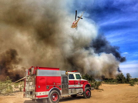 A helicopter makes a drop on a fire which broke out in Arizona and spread into California, sparking the evacuation of two recreational vehicle parks near the Havasu National Wildlife Refuge in California April 6, 2016. REUTERS/San Bernardino County Fire Department via Twitter/Handout via Reuters