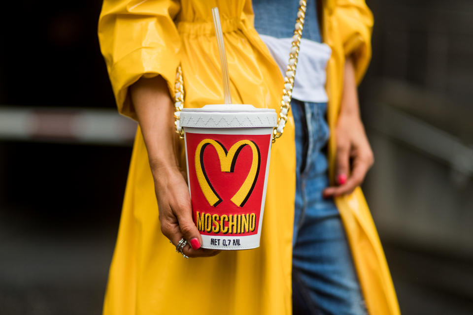 DUESSELDORF, GERMANY - AUGUST 5: Model and fashion blogger Gitta Banko wearing a long yellow patent-leather coat by Marina Hoermanseder, a white t-shirt by James Perse under a demin corsage by Marina Hoermanseder, Anglomania Diagonal Zip jeans by Vivienne Westwood, a Moschino Milk Shake shoulder bag in white and red leather from the McDonalds capsule collection, and red patent-leather Pigalle pumps by Christian Louboutin on August 5, 2017 in Duesseldorf, Germany. (Photo by Christian Vierig/Getty Images)