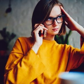 Pondering serious businesswoman in eyeglasses for vision correction looking away while calling on smartphone device and talking about solving problem.Confident young woman communicating on telephone