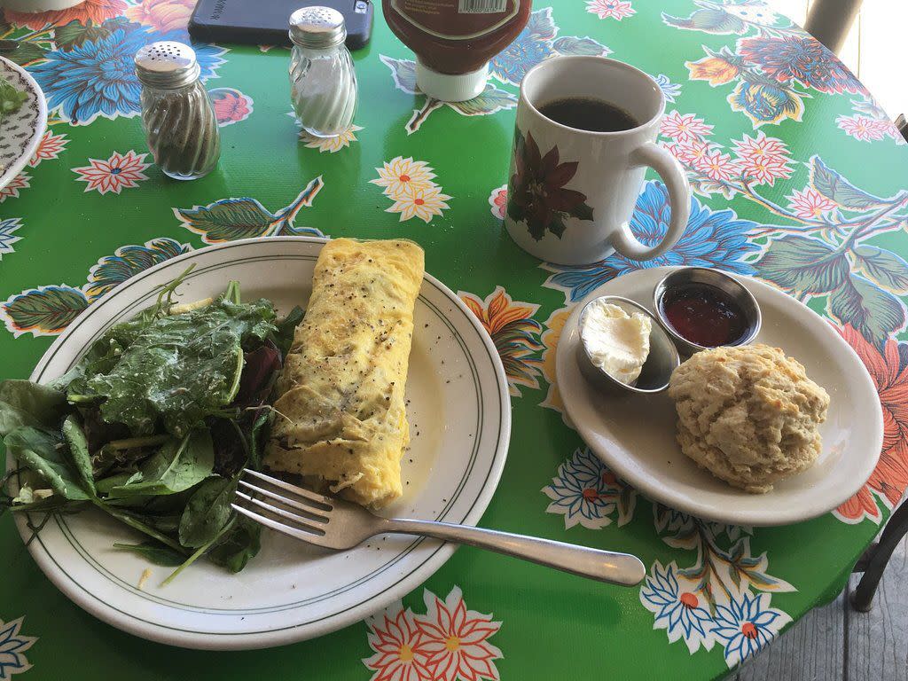 An omelet, salad, cup of coffee, and biscuit sit on a table covered in a colorful floral print at The Root Cafe in Little Rock, Arkansas.
