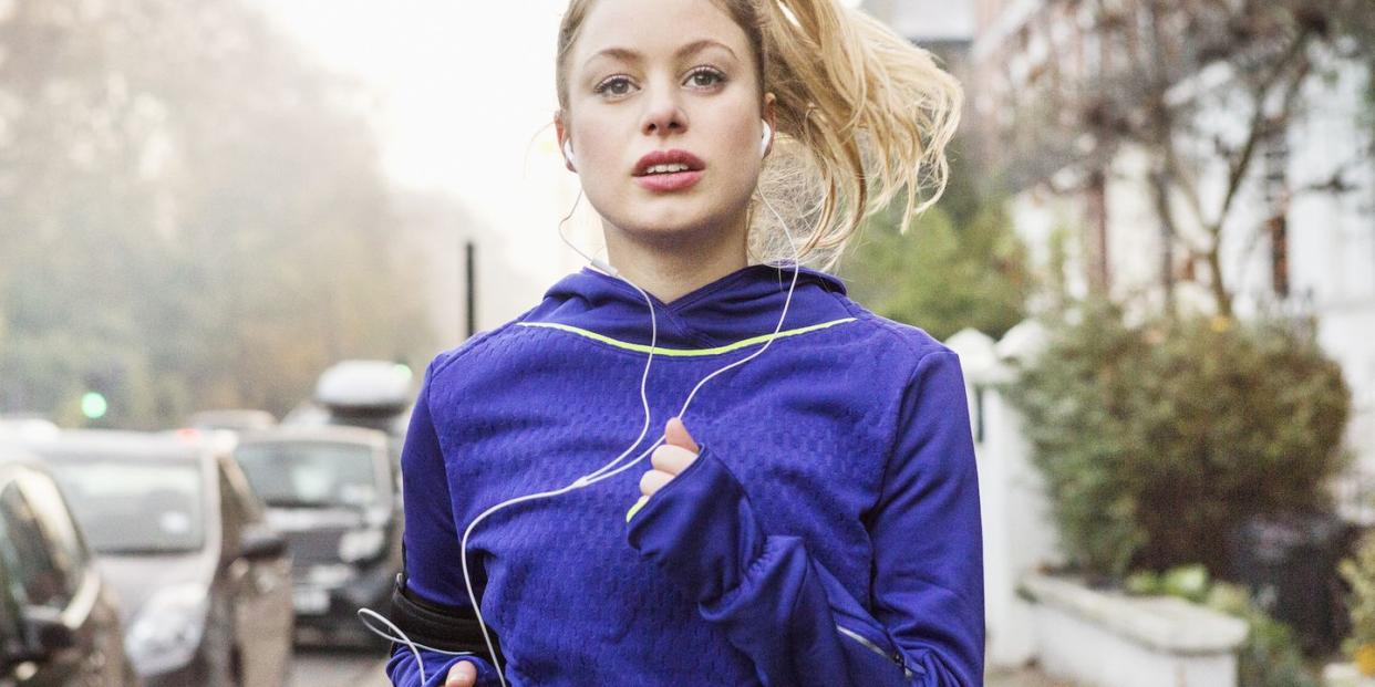 young woman jogging down the street with headphones on