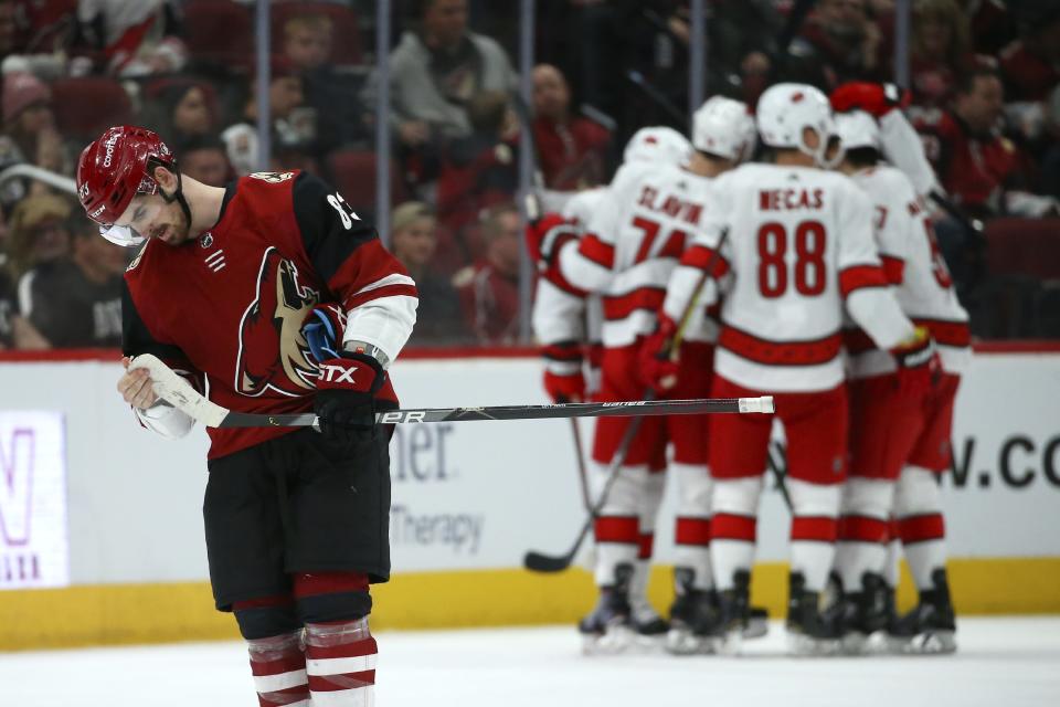 Arizona Coyotes right wing Conor Garland, left, skates back to the bench after Carolina Hurricanes defenseman Jaccob Slavin, second from left at rear, celebrates his goal with teammates, including center Martin Necas (88) and defenseman Trevor van Riemsdyk, right, during the second period of an NHL hockey game Thursday, Feb. 6, 2020, in Glendale, Ariz. (AP Photo/Ross D. Franklin)