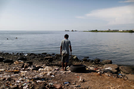 A man stands next to a pile of garbage on the shores of Lake Maracaibo in Maracaibo, Venezuela July 26, 2018. Picture taken July 26, 2018. REUTERS/Marco Bello