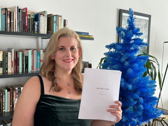 Samantha Herman holding her script while posing in front of her blue Christmas tree