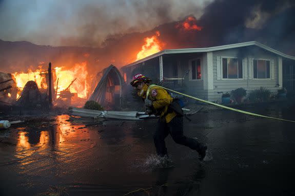 A firefighter pulls a hose to keep flames from advancing to adjacent homes while battling the Lilac fire at Rancho Monserate Country Club.