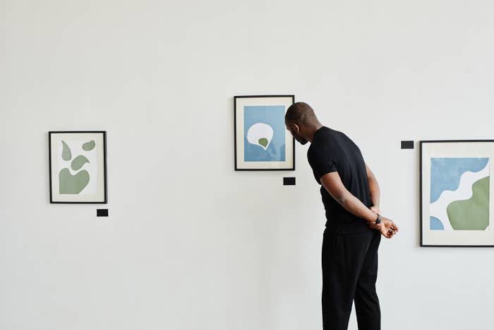 Man in black viewing abstract art displayed in frames on a white wall