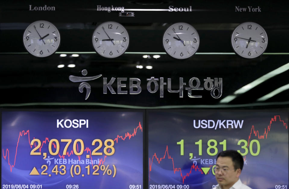 A currency trader walks by the screens showing the Korea Composite Stock Price Index (KOSPI), left, and the foreign exchange rate between U.S. dollar and South Korean won at the foreign exchange dealing room in Seoul, South Korea, Tuesday, June 4, 2019. Shares are mixed in Asia after a tumultuous session for tech shares on Wall Street.(AP Photo/Lee Jin-man)