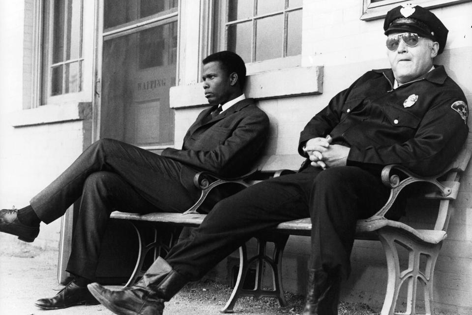 Sidney Poitier and Rod Steiger sitting on a bench ignoring one another in a scene from the film 'In The Heat Of The Night', 1967.