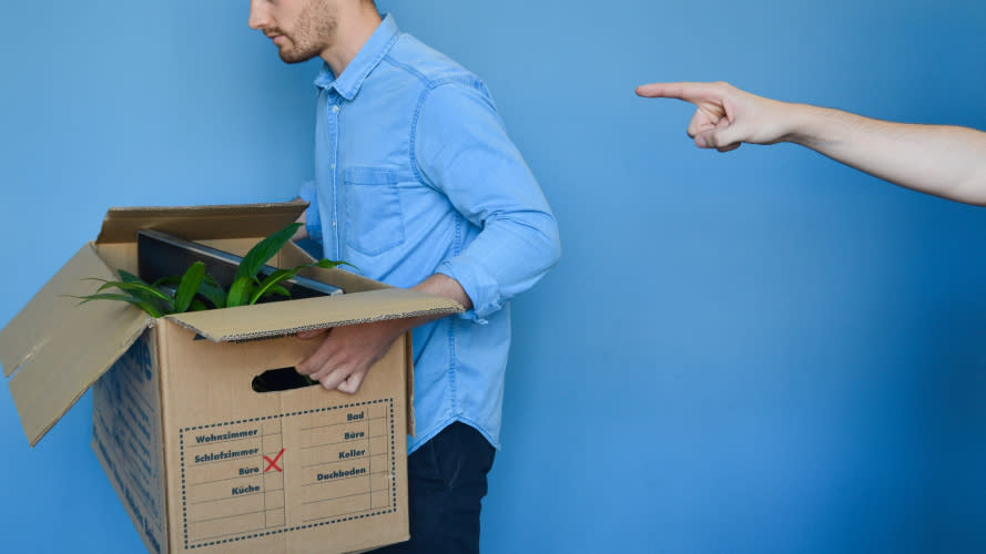 A man carrying a box of belongings as a finger points him out the door.