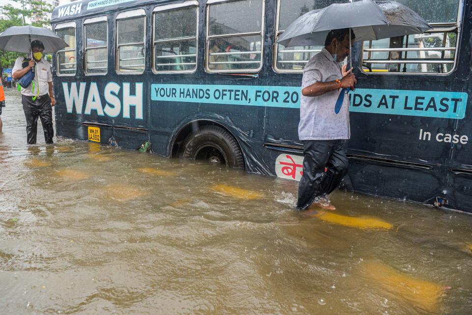 Commuters wade past a stranded bus on a flooded road during a heavy monsoon rain in Mumbai on August 4, 2020. (Photo by INDRANIL MUKHERJEE/AFP via Getty Images)