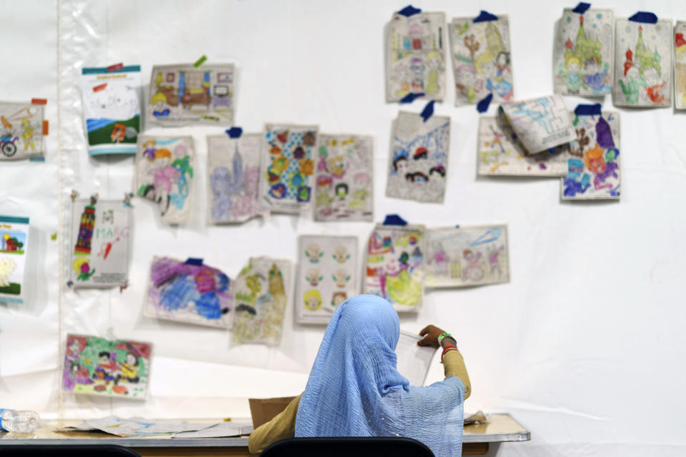 A child holds up a piece of artwork while drawing in a tent at Fort Bliss' Doña Ana Village, in New Mexico, where Afghan refugees are being housed, Friday, Sept. 10, 2021. The Biden administration provided the first public look inside the U.S. military base where Afghans airlifted out of Afghanistan are screened, amid questions about how the government is caring for the refugees and vetting them. (AP Photo/David Goldman)