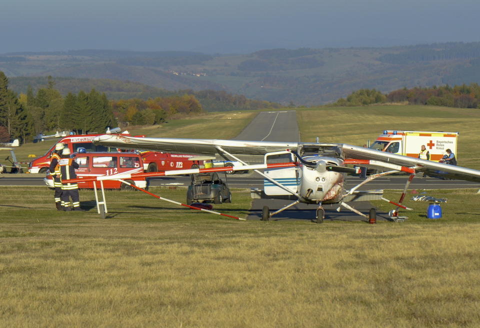 Firefighters stand beside a light aircraft near the airport in Gersfeld, Germany, Sunday, Oct. 14, 2018 after three people died after they were hit by the small plane as it attempted to take off from an aborted landing. (Martin Engel/Osthessen-News/dpa via AP)