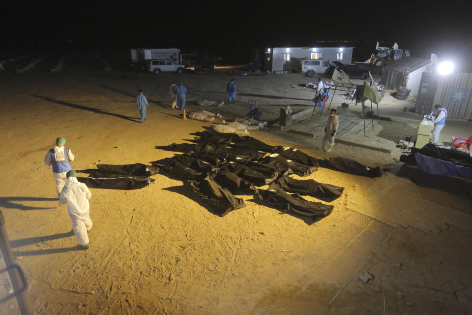 Membersof the Shiite Imam Ali brigades militia stands next to bodies during funerals of coronavirus victims at Wadi al-Salam cemetery near Najaf, Iraq, Sunday, July 19, 2020. A special burial ground near the Wadi al-Salam cemetery has been created specifically for COVID-19 victims since rejections of such burials have continued in Baghdad cemeteries and elsewhere in Iraq. (AP Photo/Anmar Khalil)