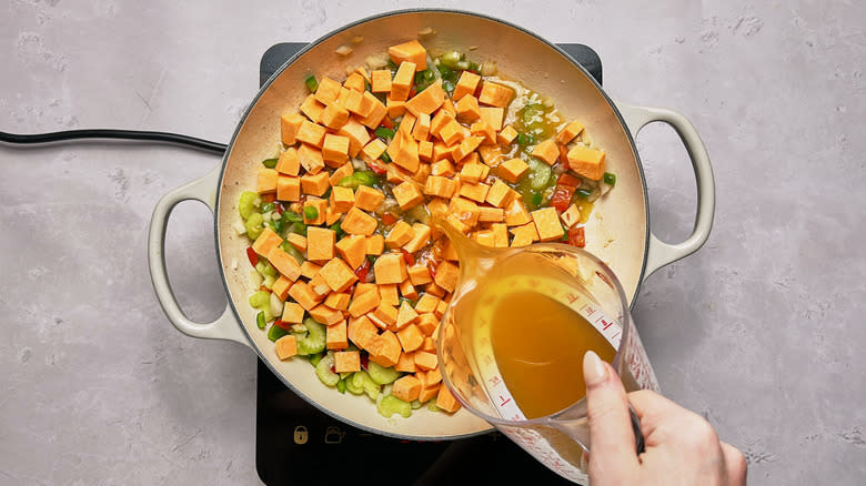 pouring broth into skillet with sweet potatoes