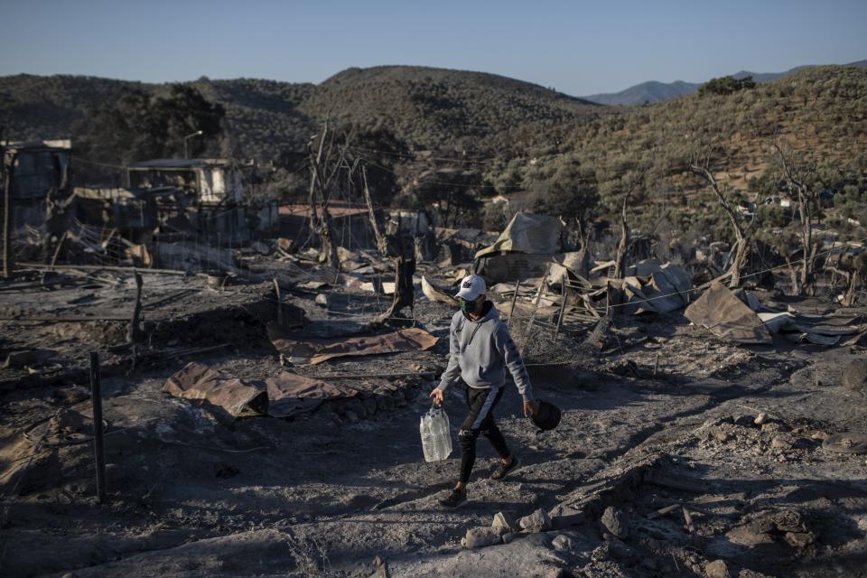 A migrant carries water as he walks in the burned Moria refugee camp on the northeastern island of Lesbos, Greece, Thursday, Sept. 10, 2020. A second fire in Greece's notoriously overcrowded Moria refugee camp destroyed nearly everything that had been spared in the original blaze, Greece's migration ministry said Thursday, leaving thousands more people in need of emergency housing. (AP Photo/Petros Giannakouris)