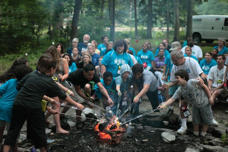 Children and adults are gathered around a bonfire roasting marshmallows.