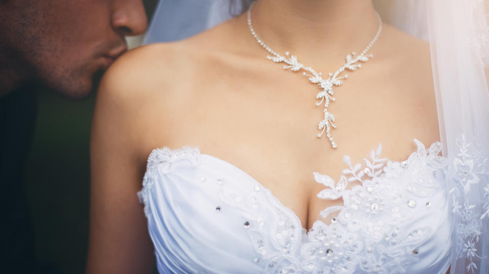 Close-up of female breasts in the low-necked dress and the groom kissing a bride's shoulder.