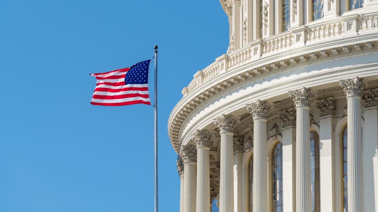  An American flag flying outside the US Capitol building against a blue sky. 