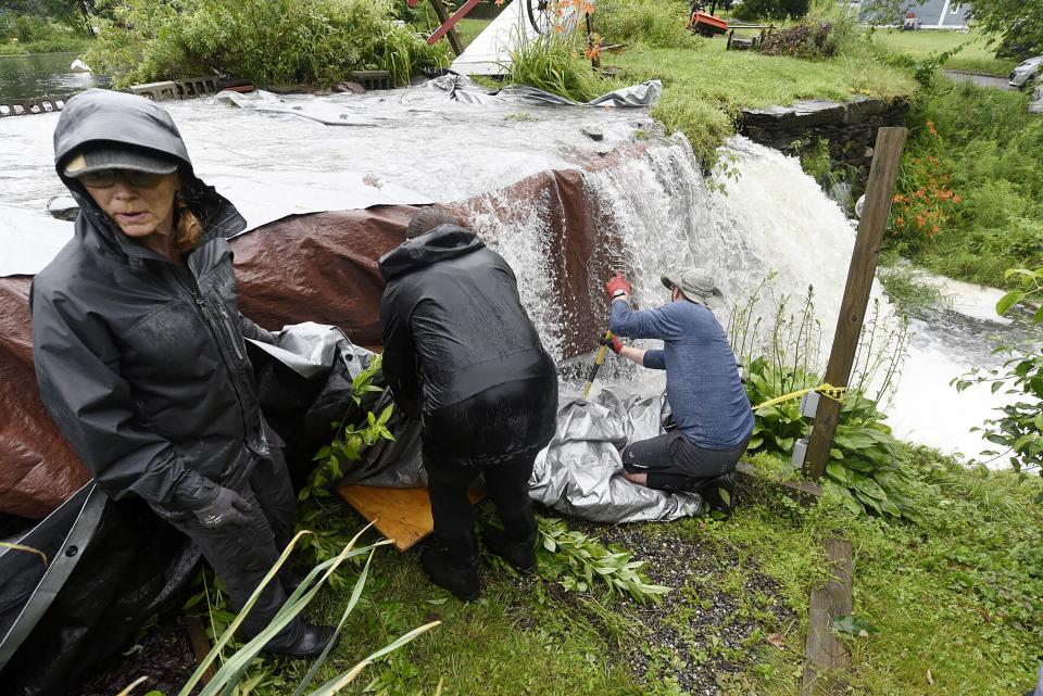 Meg Dawkins, left, and other community members, use tarps to keep the Curtis Pond dam from getting undermined Monday, July 10, 2023 in Calais, Vt. (Jeb Wallace-Brodeur/The Times Argus via AP)