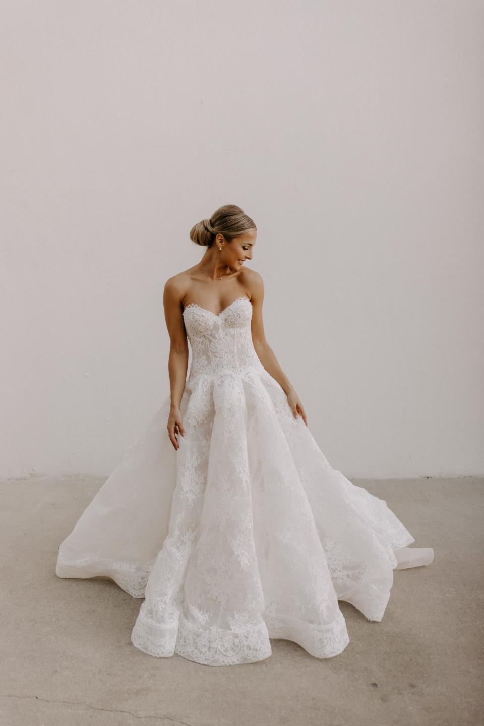 A woman stands in a wedding dress and looks over her shoulder.