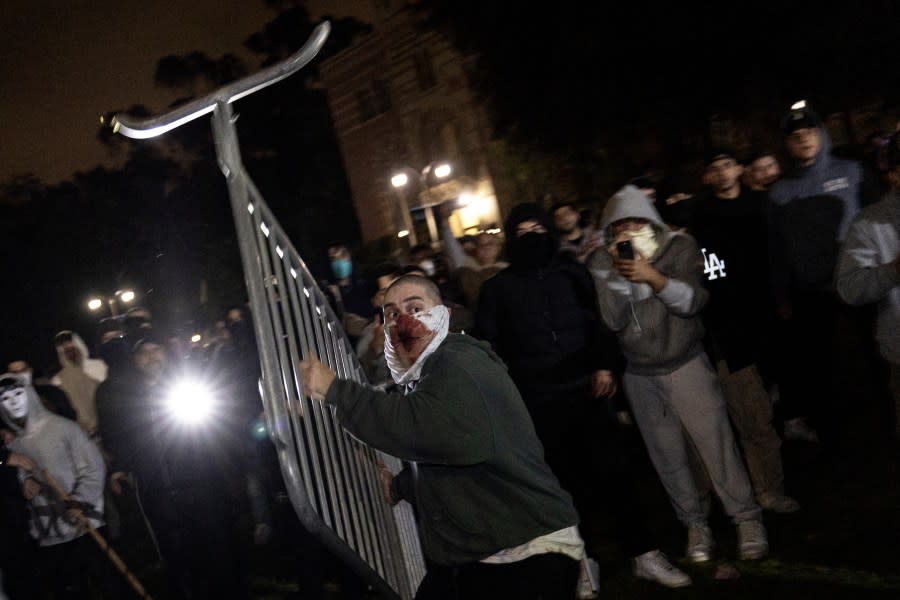 A counter protester throws a fence at pro-Palestinian protesters next to their encampment set up on on the campus of the University of California Los Angeles (UCLA), as clashes erupt in Los Angeles on May 1, 2024. Clashes broke out on May 1, 2024 around pro-Palestinian demonstrations at the University of California, Los Angeles, as universities around the United States struggle to contain similar protests on dozens of campuses. (Photo by ETIENNE LAURENT / AFP) (Photo by ETIENNE LAURENT/AFP via Getty Images)