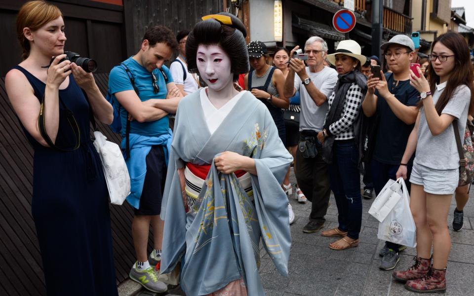 Tourists take photos of a geisha walking in the Gion district of Kyoto, Japan