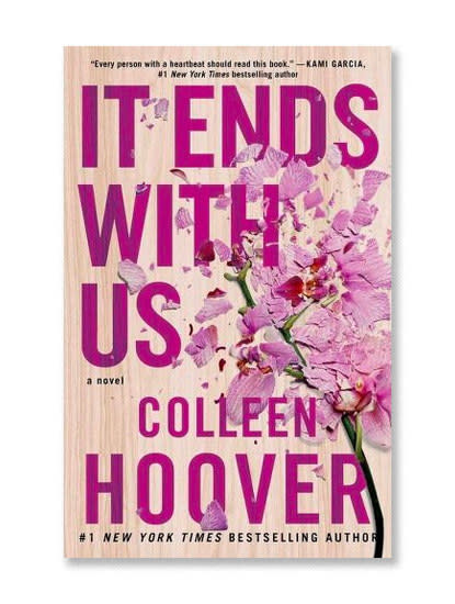 Colleen Hoover's "It Ends With Us" cover. It is a light woodgrain and a flower laying on it, looking crushed and torn.