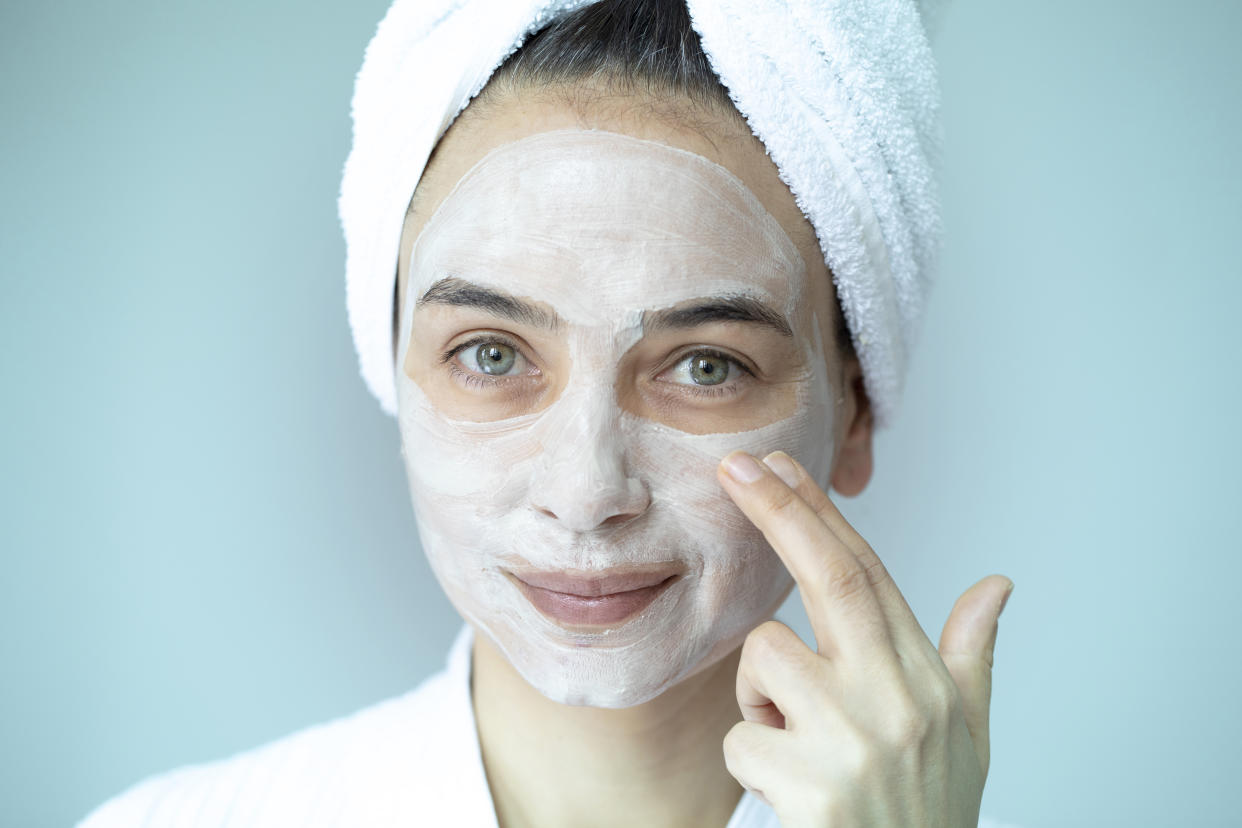 A woman with her hair up in a towel applies cream to her face.