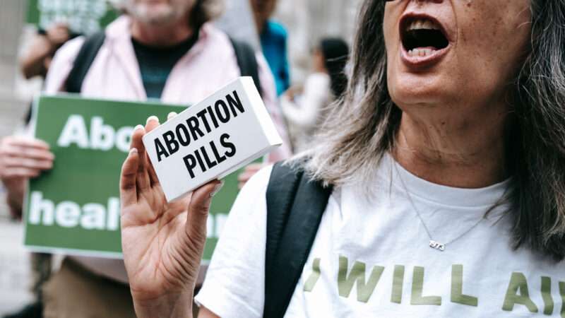 woman at protest holding box that says "abortion pils"