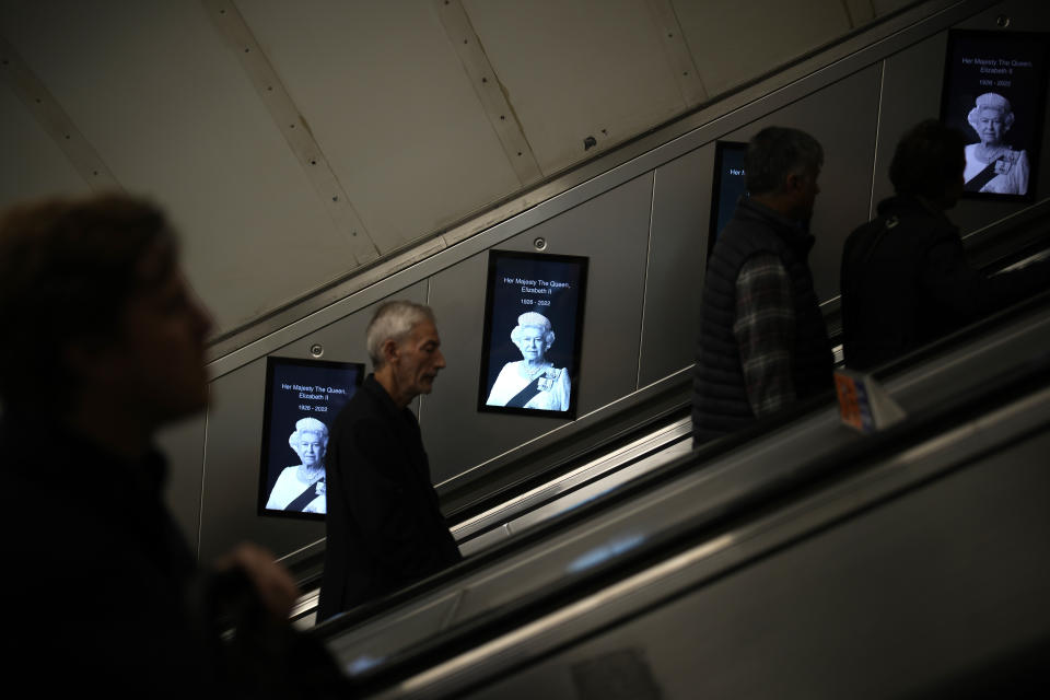FILE - Commuters walk past photos of the late Queen Elizabeth II in the London subway, Saturday, Sept. 10, 2022. On morning television, the moment was singularly somber — the departure of the hearse bearing the flag-draped coffin of Queen Elizabeth II. But at the very same hour, as fans in shorts and Ray-Bans streamed into London's Oval stadium for a long-anticipated cricket match, you wouldn't have guessed the country was preparing for the most royal of funerals. (AP Photo/Christophe Ena, File)