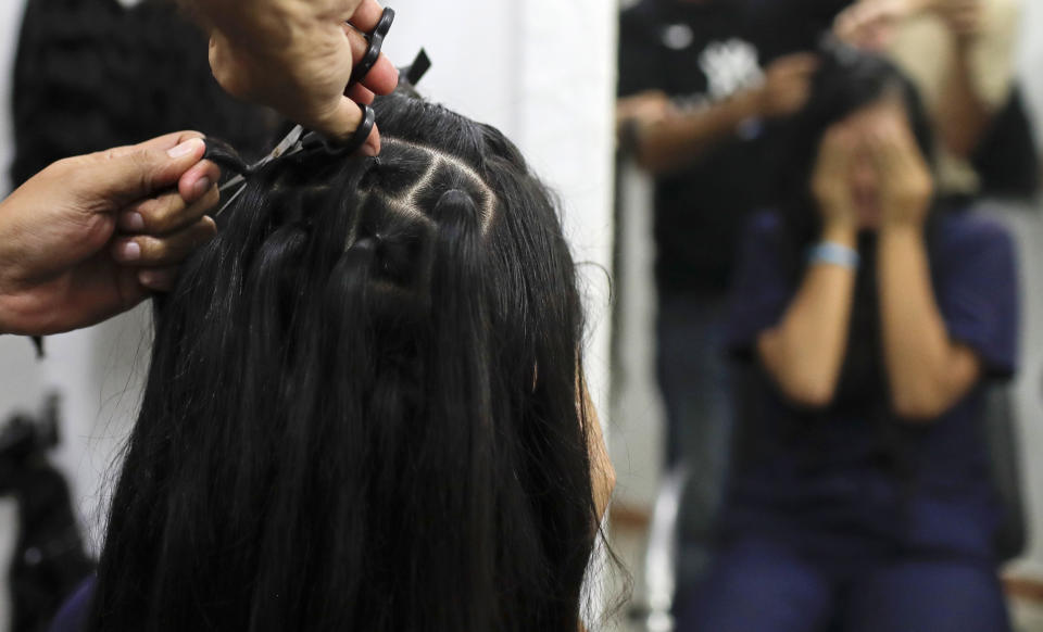 Valery Díaz covers her face as she gets her hair cut off for $100 at a beauty salon in Caracas, Venezuela, Friday, April 5, 2019. Due to lack of water, shampoo and conditioner, Díaz changed her weekly personal hygiene habits and started making and selling bracelets to buy soap and makeup. (AP Photo/Natacha Pisarenko)