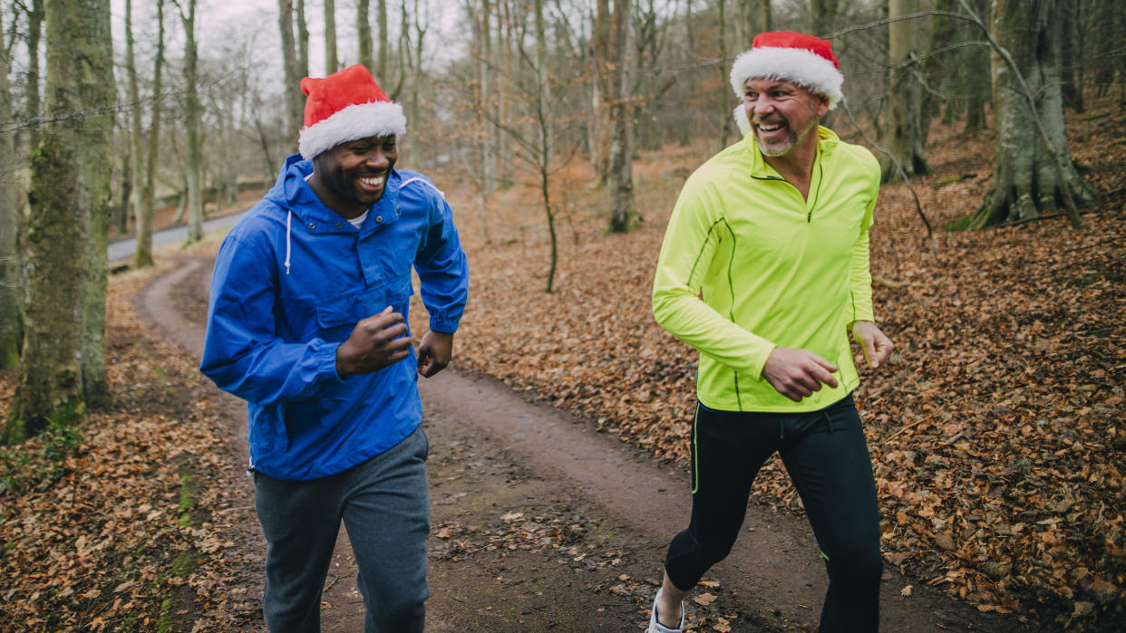  Two men running in woodland wearing Santa hats. 