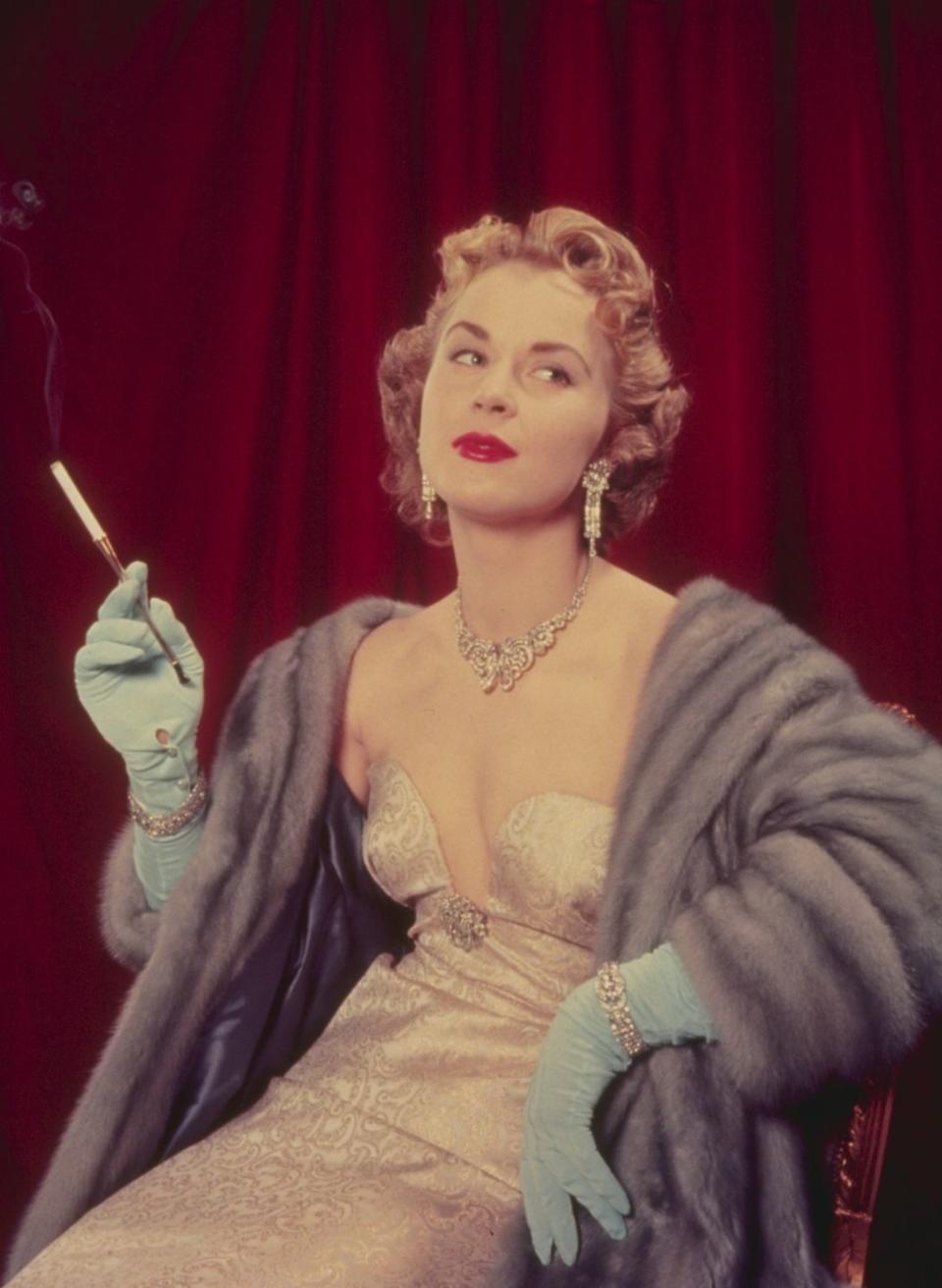 <p>A woman wearing an ornate evening gown with opera gloves and a pelted fur stole. </p>