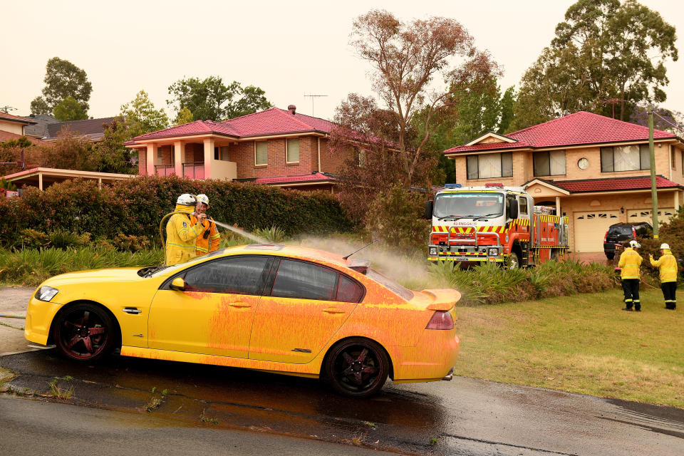 Picture of fire-fighters hosing down cars and driveways to remove the fire retardant, which was used to help ease fires in Sydney's north on Tuesday.