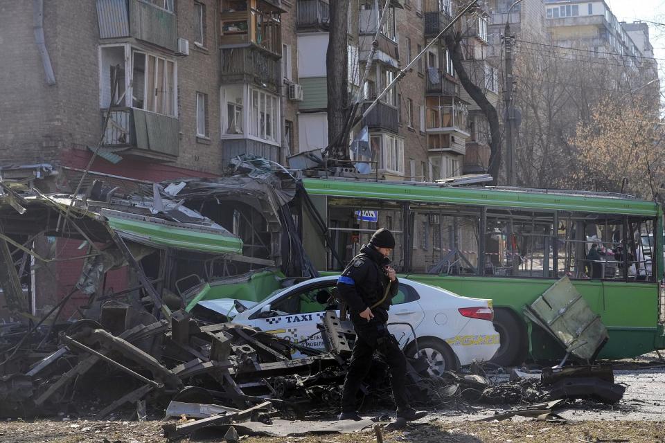 Ein ukrainischer Soldat vor einem zerstörten Trolleybus und Taxi nach einem russischen Bombenangriff, Kiew, 14. März 2022