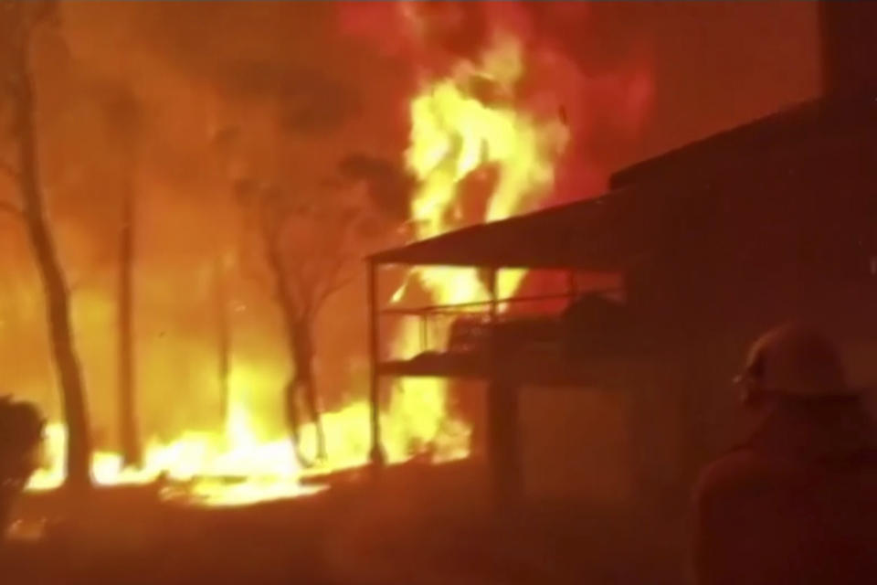 In this image made from video taken and provided by NSW RFS via their twitter account, a firefighter sprays water on a fire moving closer to a home in Blackheath, New South Wales state, Australia Sunday, Dec. 22, 2019. Prime Minister Scott Morrison on Sunday apologized for taking a family vacation in Hawaii as deadly bushfires raged across several states, destroying homes and claiming the lives of two volunteer firefighters.(Twitter@NSWRFS via AP)