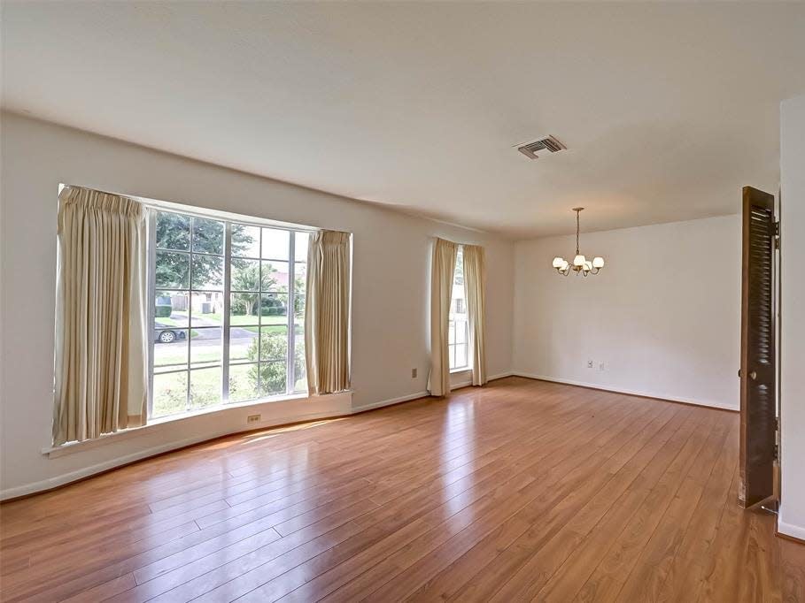 the empty living space with laminate floors and two windows in a house for sale in houston