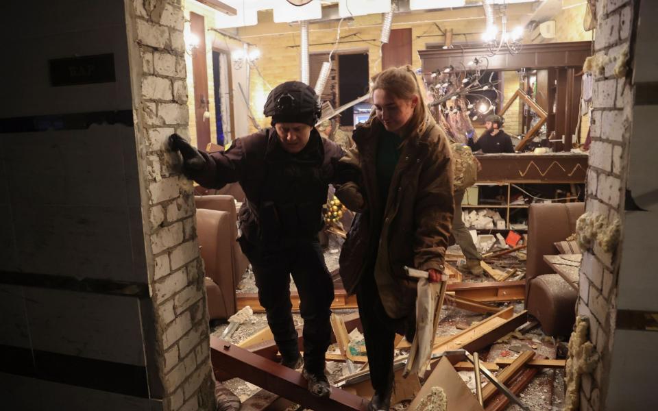 A policeman helps a woman leave the damaged hotel after two Russian S-300 missile strikes