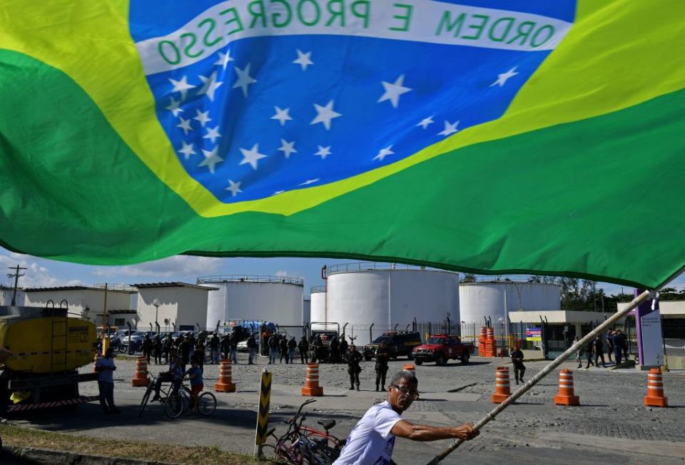 TOPSHOT - A protestor waves the Brazilian national flag outside the Duque de Caxias refinery in metroplitan Rio de Janeiro, Brazil, on May 28, 2018, where soldiers have been deployed to guarantee the safe transport of fuel for essential services. - A truckers' strike paralyzing fuel and food deliveries across Brazil entered an eighth day Monday but with hopes of relief after unpopular President Michel Temer caved in to the strikers' key demand. Road blockages by truckers remained in place across 21 of the country's 27 states, G1 news site reported. (Photo by Carl DE SOUZA / AFP)        (Photo credit should read CARL DE SOUZA/AFP via Getty Images)