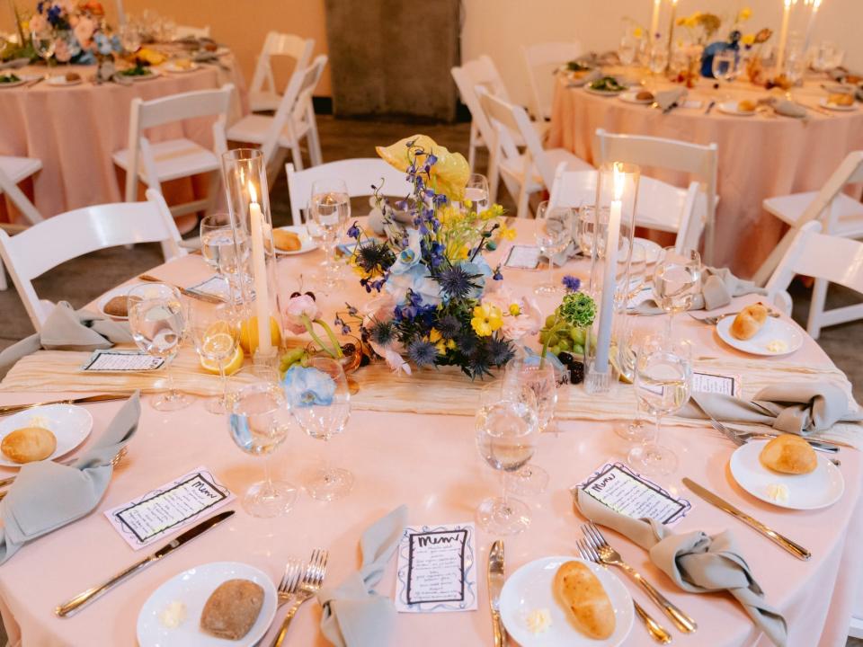 Flowers sit on a table with pink tablecloth and several place settings.