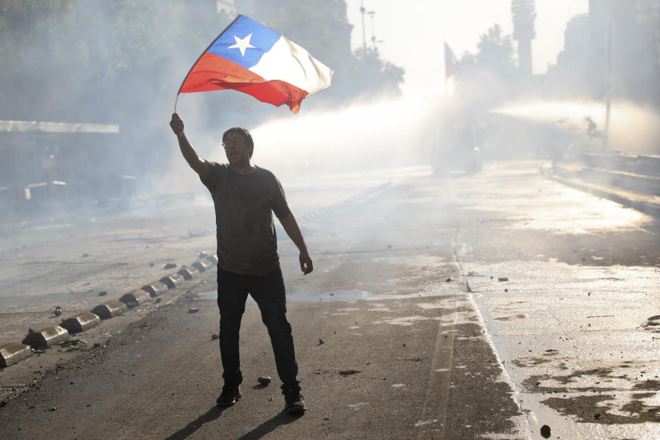 An anti-government protester waves a national flag in Santiago, Chile, Tuesday, Oct. 29, 2019. Chileans gathered Tuesday for a 12th day of demonstrations that began with youth protests over a subway fare hike and have become a national movement demanding greater socio-economic equality and better public services in a country long seen as an economic success story. (AP Photo/Rodrigo Abd)