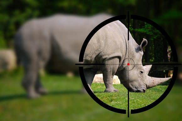 A rhinoceros grazing on grass and standing in the crosshairs of a telescope.