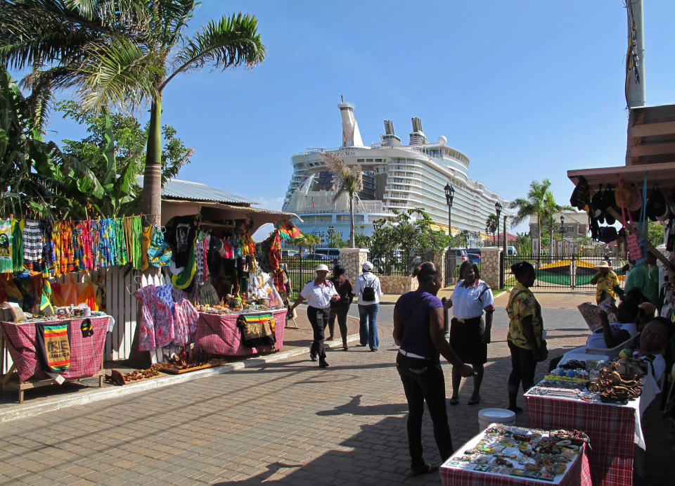 In this Sept. 26, 2012 photo, the Royal Caribbean's Allure of the Seas cruise ship is docked in Falmouth, northern Jamaica as street vendors sell clothes, souvenirs and other goods to tourists. Trade groups say the flourishing cruise ship industry injects about $2 billion a year into the economies of the Caribbean, the world’s No. 1 cruise destination, but critics complain that it produces relatively little local revenue because so many passengers dine, shop and purchase heavily marked-up shore excursions on the boats or splurge at international chain shops on the piers. (AP Photo/David McFadden)