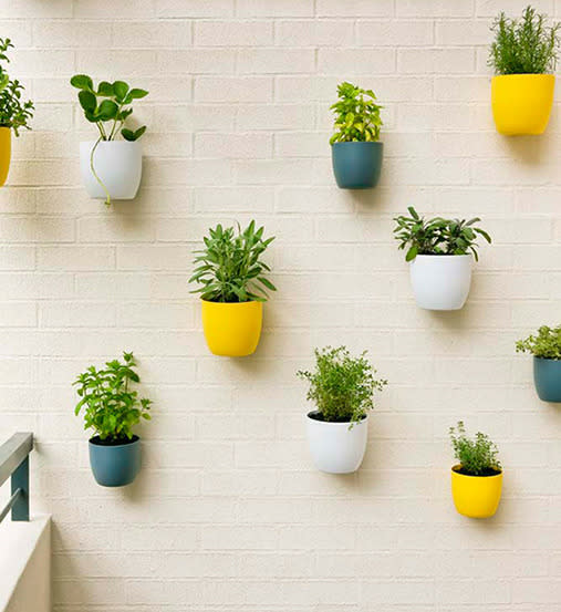 There's no need to buy vertical garden kits - you can simply secure your own pots to the wall. Here, herbs have been planted in different coloured pots and attached to the wall with concrete screws. <br><br>Click here for <a rel="nofollow" href="https://au.lifestyle.yahoo.com/better-homes-gardens/gardening/h/24587458/how-to-make-a-potted-wall/" data-ylk="slk:how to make a potted wall;elm:context_link;itc:0;sec:content-canvas" class="link ">how to make a potted wall</a>