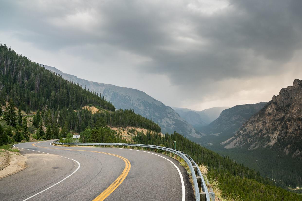 Road curving around mountain on Beartooth Highway, Montana, with mountains and dramatic clouds in the background