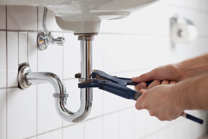 person removing sink trap under sink to unclog the drain