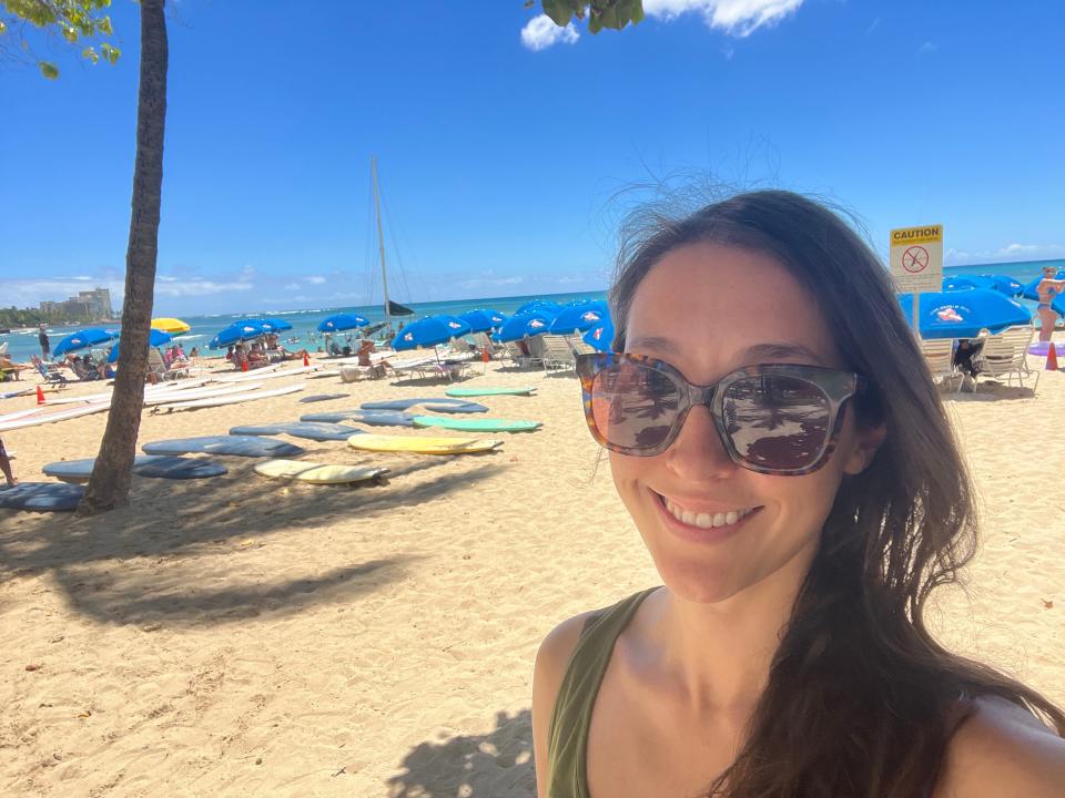 A woman wearing sunglasses takes a selfie on a tropical beach.