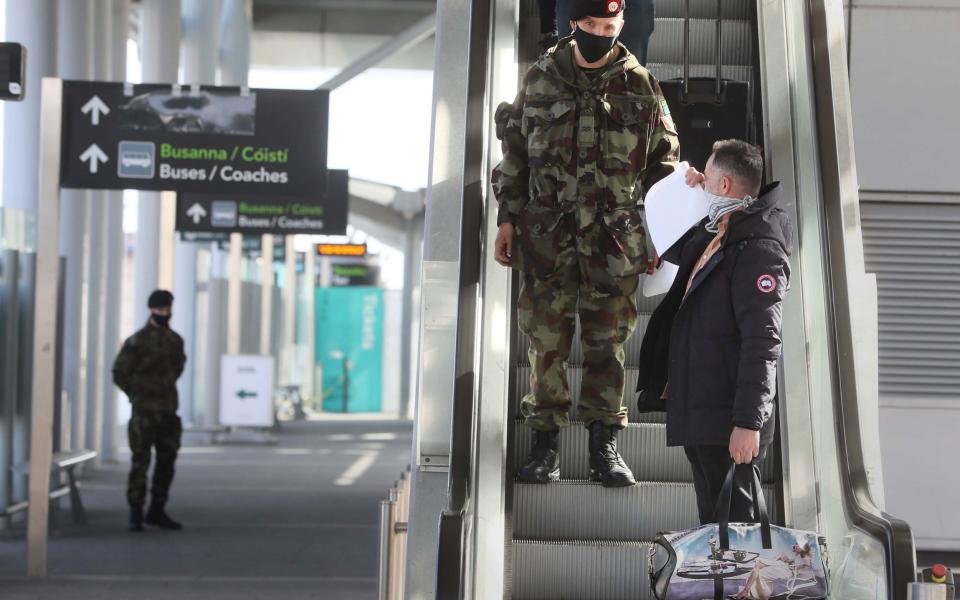 A passenger is escorted to a coach by a member of the defence forces after arriving at Dublin Airport - Brian Lawless/PA