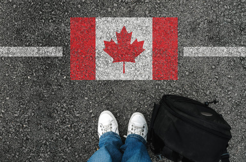 a man with a shoes and backpack is standing on asphalt next to flag of Canada and border